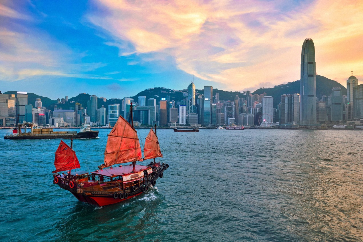 Traditional Chinese junk with red sails on Victoria Harbour before the Hong Kong skyline