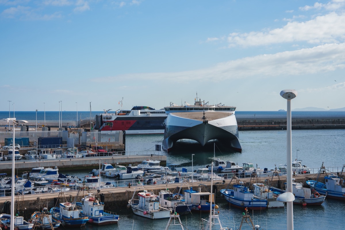 A modern high-speed catamaran moored in Tarifa ferry port, surrounded by fishing boats