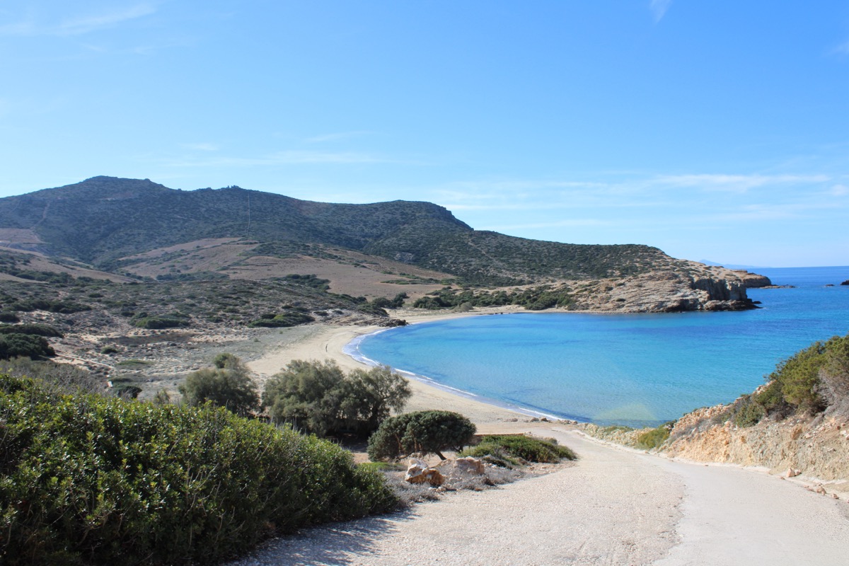 Einsamer Sandstrand in einer geschützten Bucht auf Kreta, umgeben von trockenen Hügeln mit Macchia-Vegetation