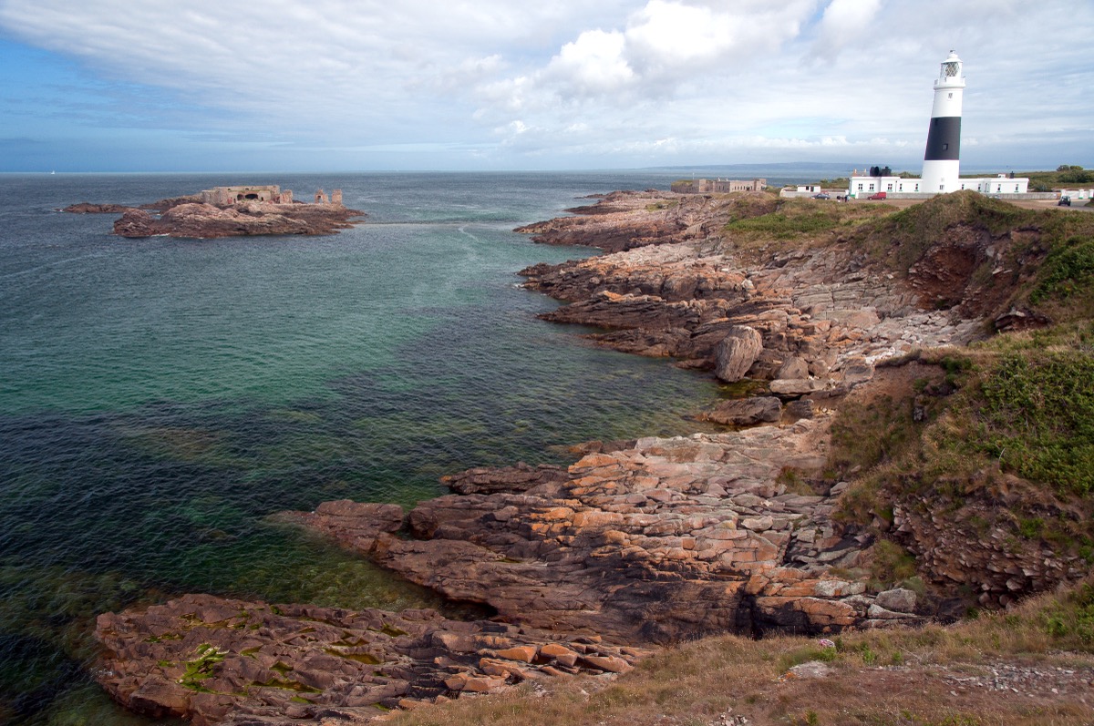Rocky coastline of Alderney with the black-and-white Quesnard lighthouse