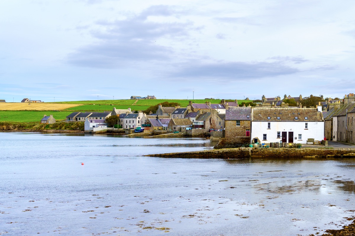 Idyllisches Fischerdorf St Margaret's Hope auf den Orkney-Inseln mit alten Steinhäusern direkt am ruhigen Meeresarm