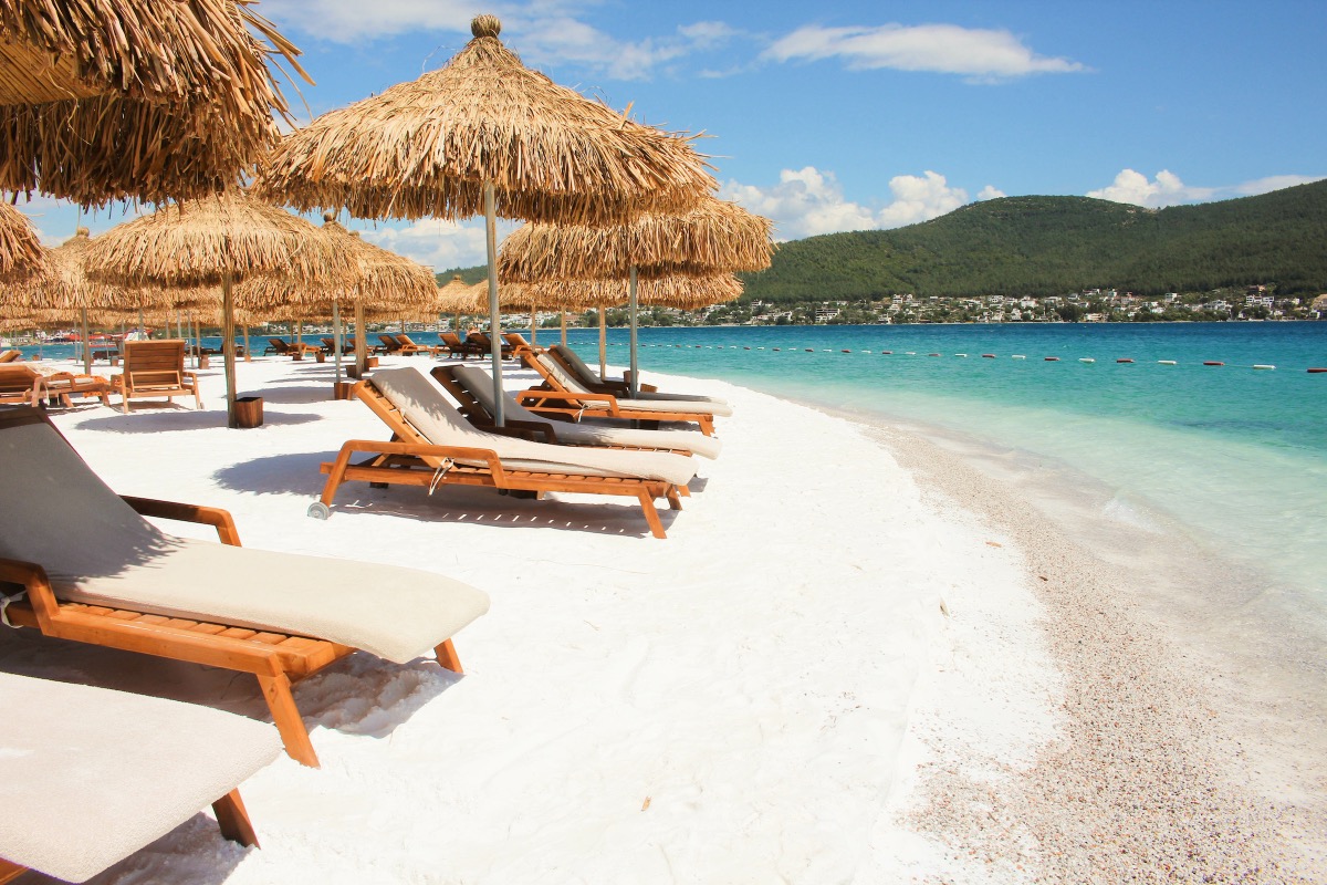 White sandy beach with wooden sun loungers and thatched roofs on the turquoise Mediterranean
