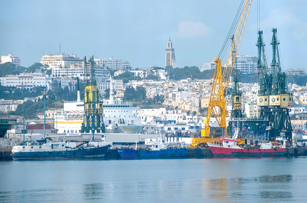 View from the sea of Tangier's harbor with yellow industrial cranes, a cruise ship and the white medina on the hillside